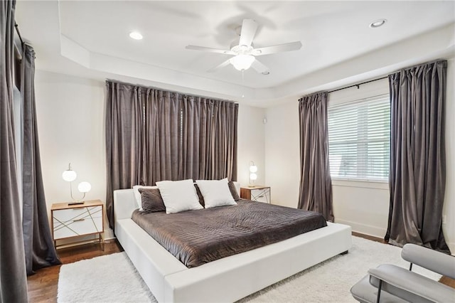 bedroom with wood-type flooring, a tray ceiling, and ceiling fan