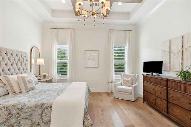 bedroom featuring a notable chandelier, light wood-type flooring, a tray ceiling, and multiple windows