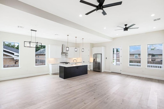 kitchen featuring pendant lighting, stainless steel fridge with ice dispenser, a kitchen island with sink, ceiling fan with notable chandelier, and white cabinets