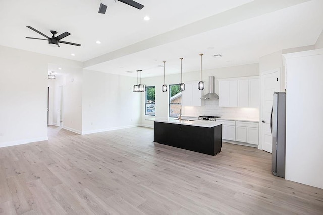 kitchen with wall chimney exhaust hood, an island with sink, white cabinetry, stainless steel refrigerator, and sink