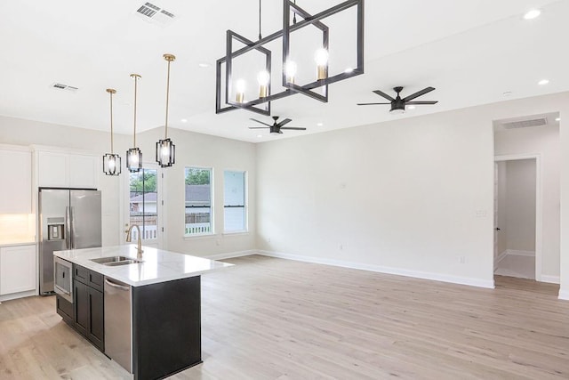 kitchen featuring sink, light hardwood / wood-style flooring, ceiling fan with notable chandelier, a center island with sink, and appliances with stainless steel finishes