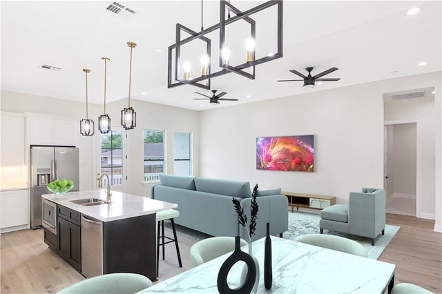 living room featuring ceiling fan with notable chandelier, light wood-type flooring, and sink