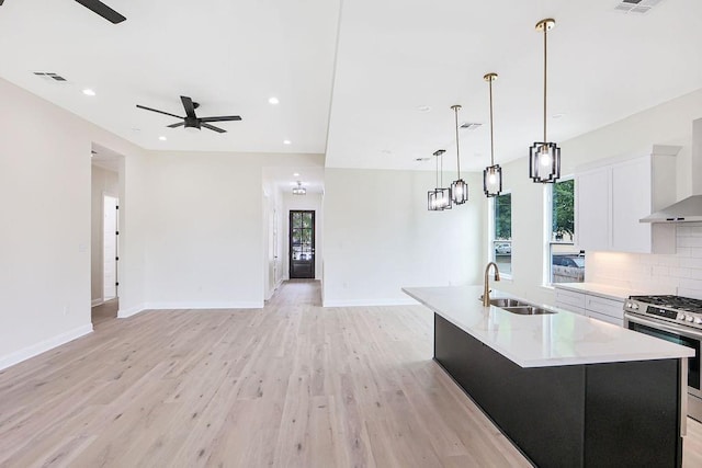 kitchen with pendant lighting, an island with sink, gas stove, white cabinets, and sink