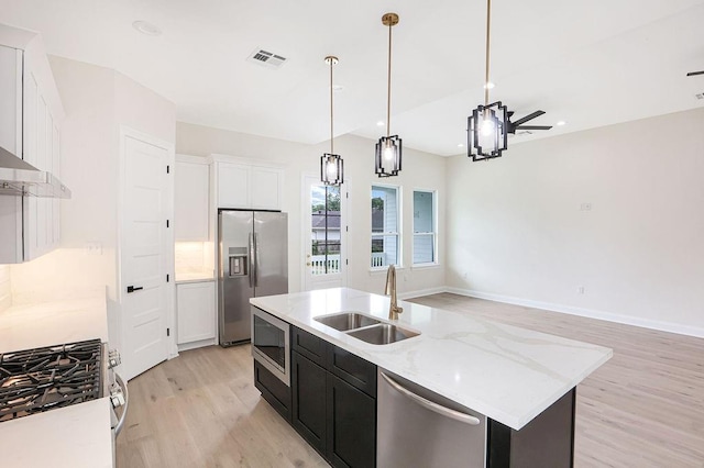 kitchen with decorative light fixtures, appliances with stainless steel finishes, a kitchen island with sink, and white cabinetry