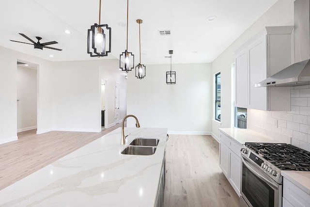 kitchen with stainless steel gas stove, wall chimney exhaust hood, hanging light fixtures, and sink