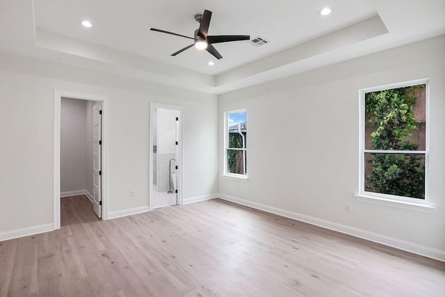 unfurnished bedroom with a walk in closet, a raised ceiling, ceiling fan, and light hardwood / wood-style flooring