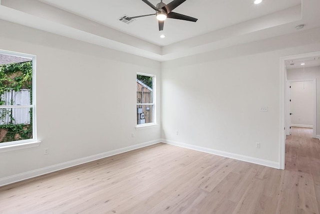 unfurnished room with light hardwood / wood-style floors, ceiling fan, and a tray ceiling