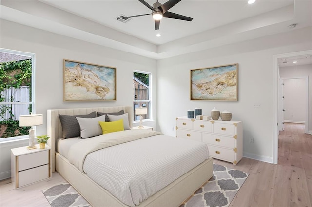 bedroom featuring ceiling fan, light hardwood / wood-style flooring, and a tray ceiling