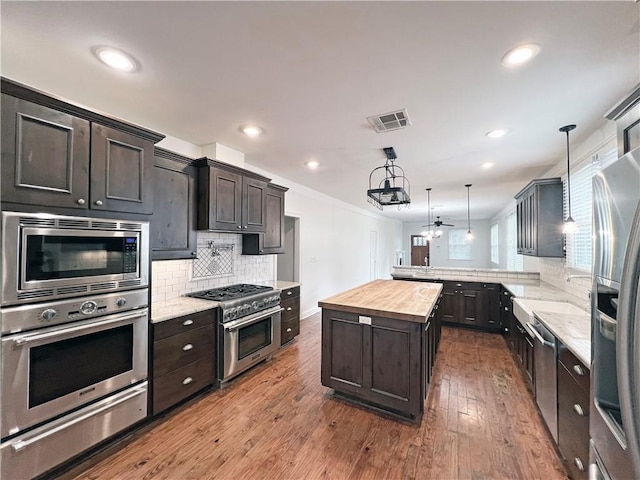 kitchen featuring a center island, hanging light fixtures, tasteful backsplash, butcher block countertops, and stainless steel appliances