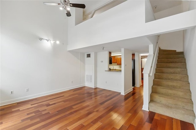 unfurnished living room with hardwood / wood-style floors, ceiling fan, and a high ceiling