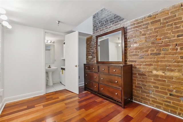 bedroom with ensuite bath, sink, brick wall, and hardwood / wood-style flooring