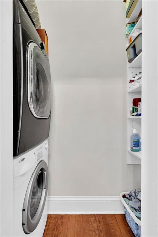 clothes washing area with stacked washer and dryer and hardwood / wood-style flooring