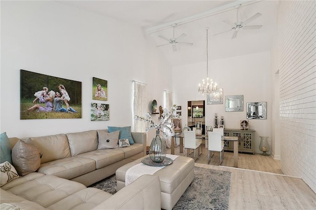 living room featuring high vaulted ceiling, brick wall, light wood finished floors, and ceiling fan with notable chandelier