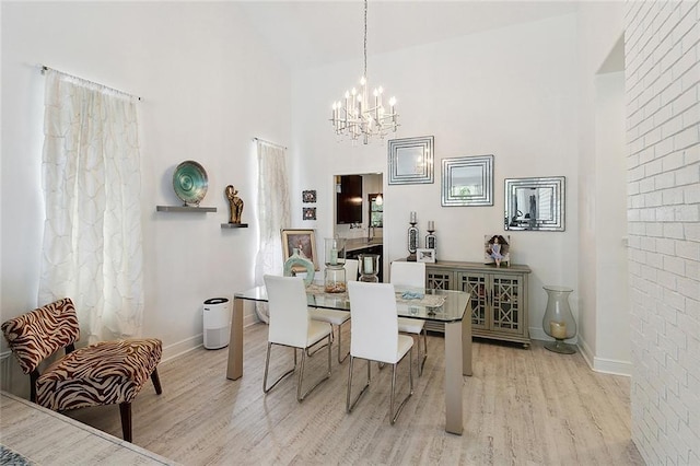 dining space featuring baseboards, a high ceiling, light wood-type flooring, and an inviting chandelier