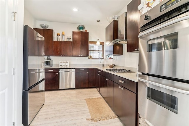 kitchen featuring light wood-style flooring, stainless steel appliances, hanging light fixtures, light countertops, and wall chimney exhaust hood