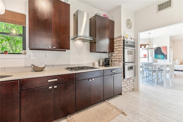 kitchen featuring visible vents, stainless steel appliances, light countertops, wall chimney range hood, and pendant lighting