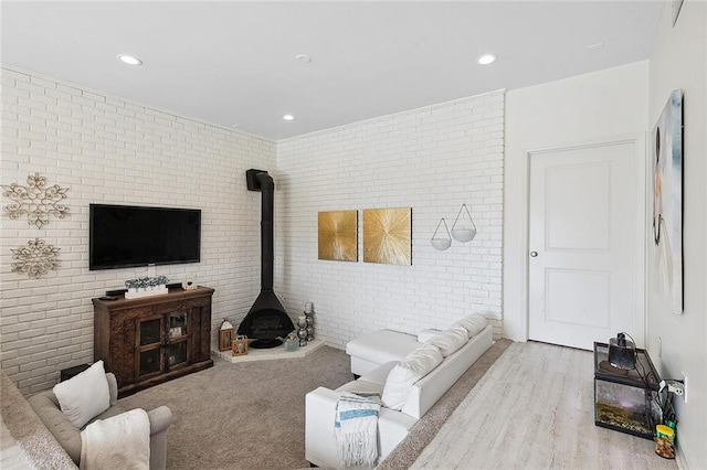 living area featuring a wood stove, light wood-style floors, brick wall, and recessed lighting