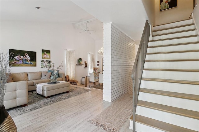 living area featuring stairway, ceiling fan, brick wall, wood finished floors, and high vaulted ceiling