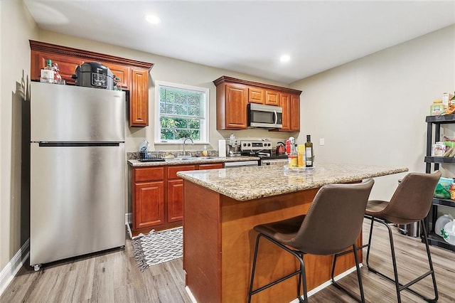 kitchen with light stone countertops, sink, stainless steel appliances, a kitchen bar, and light wood-type flooring