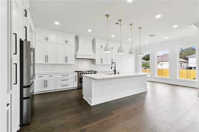 kitchen featuring premium range hood, high end appliances, white cabinets, hanging light fixtures, and an island with sink