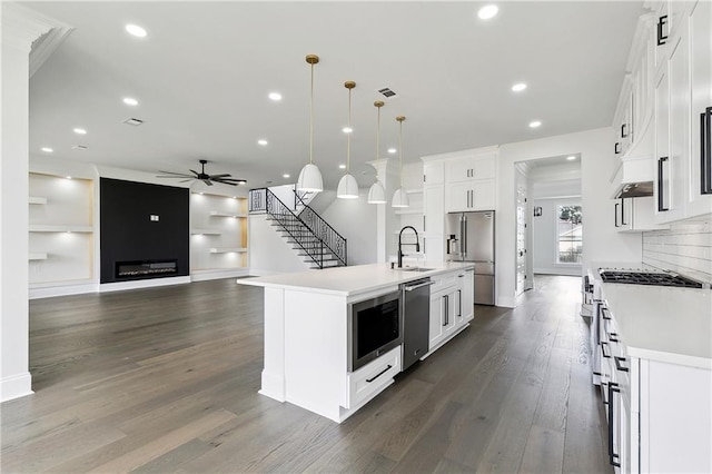 kitchen featuring a center island with sink, white cabinets, high quality appliances, and hanging light fixtures