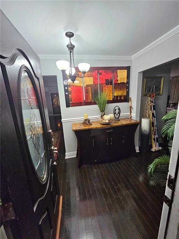 interior space with an inviting chandelier, crown molding, and dark wood-type flooring