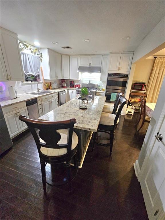 kitchen with a center island, sink, light stone counters, white cabinetry, and stainless steel appliances