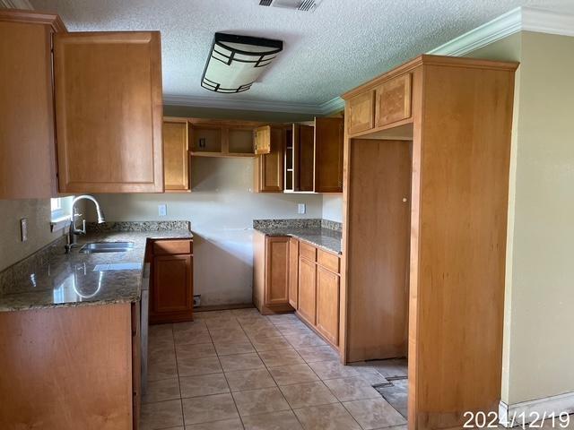 1809 W Frisco Dr, La Place, LA 70068 - kitchen featuring sink, dark stone countertops, ornamental molding, a textured ceiling, and light tile patterned floors