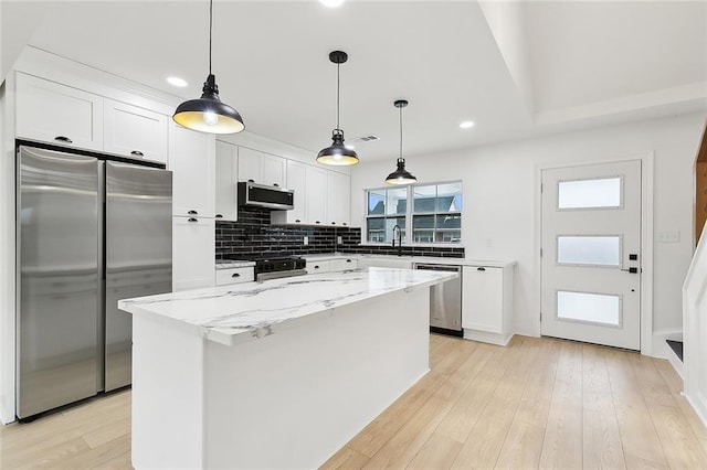 kitchen with white cabinetry, a kitchen island, light stone countertops, and appliances with stainless steel finishes