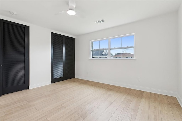 unfurnished bedroom with light wood-type flooring, ceiling fan, and multiple closets