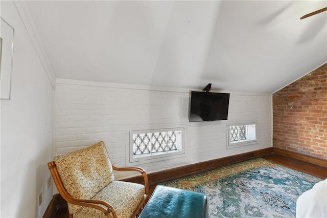 living area with wood-type flooring, vaulted ceiling, a wealth of natural light, and brick wall