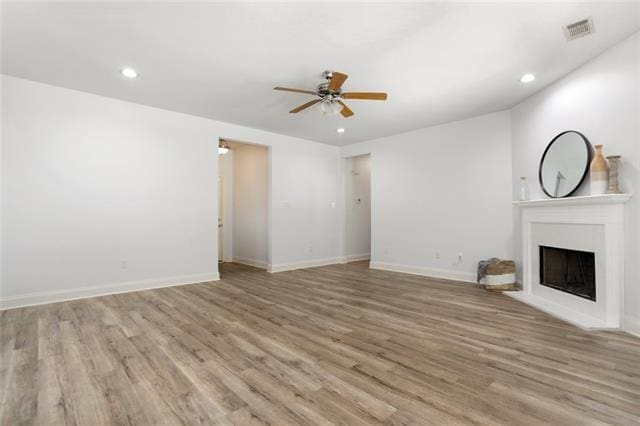 unfurnished living room featuring ceiling fan, a fireplace, visible vents, baseboards, and light wood-type flooring