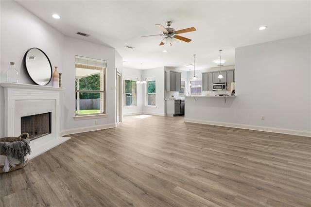 unfurnished living room with baseboards, visible vents, a fireplace with raised hearth, ceiling fan, and wood finished floors