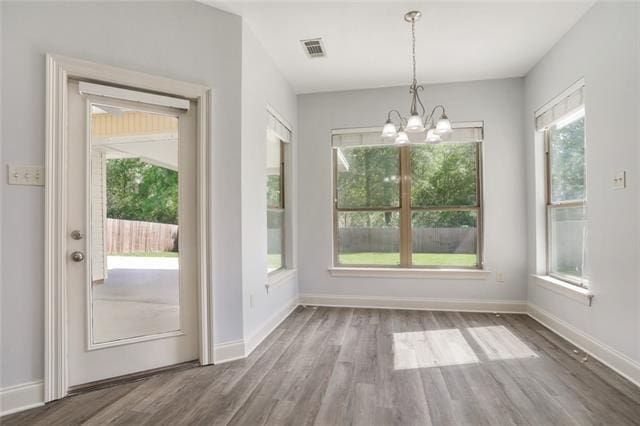 unfurnished dining area featuring a notable chandelier, baseboards, visible vents, and wood finished floors