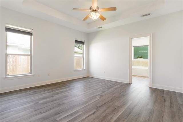 empty room with baseboards, visible vents, a raised ceiling, ceiling fan, and dark wood-type flooring