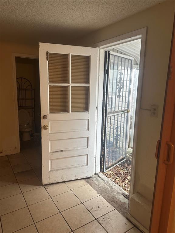 doorway featuring light tile patterned flooring, a healthy amount of sunlight, and a textured ceiling