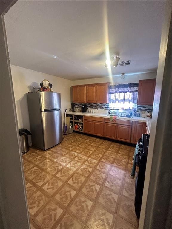 kitchen with tasteful backsplash, stainless steel fridge, light parquet floors, and range