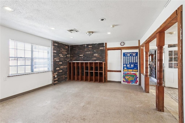 unfurnished living room with a textured ceiling and brick wall