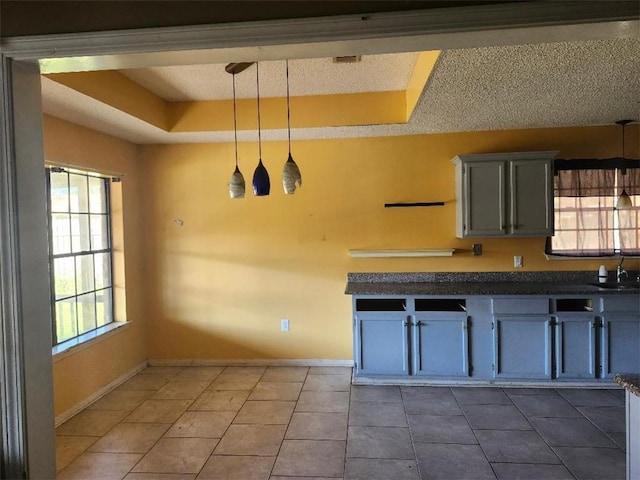 kitchen with a tray ceiling, gray cabinetry, dark tile patterned floors, and pendant lighting