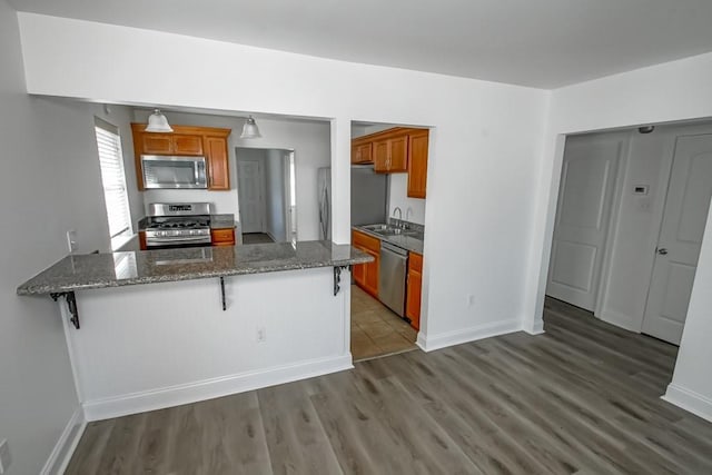 kitchen featuring brown cabinetry, a breakfast bar area, a peninsula, stainless steel appliances, and a sink