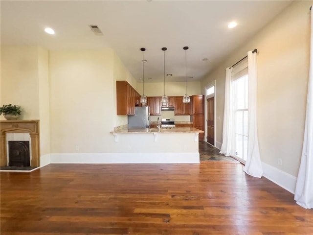 kitchen featuring kitchen peninsula, light stone counters, stainless steel appliances, pendant lighting, and dark hardwood / wood-style floors