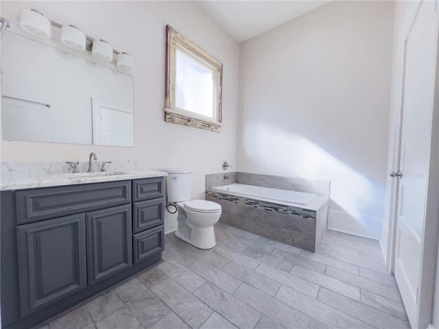 bathroom with tiled tub, vanity, and toilet