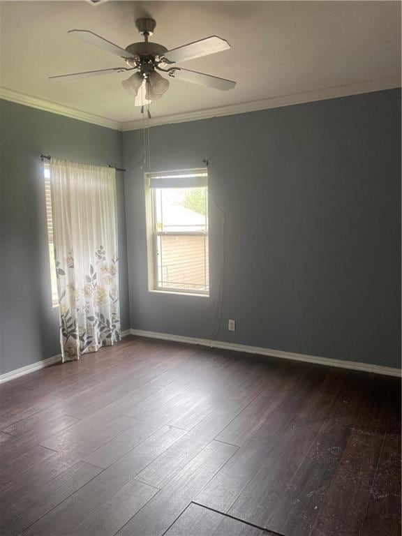 empty room featuring crown molding, baseboards, ceiling fan, and dark wood finished floors