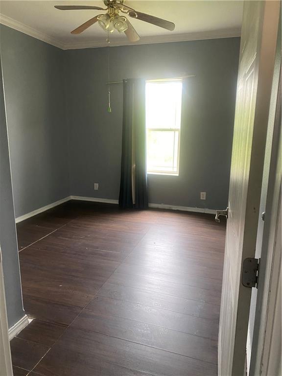 empty room with baseboards, crown molding, ceiling fan, and dark wood-type flooring