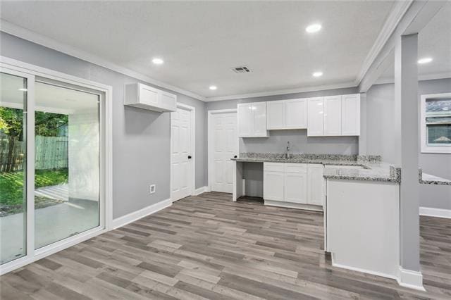 kitchen featuring hardwood / wood-style flooring, white cabinetry, crown molding, and light stone counters