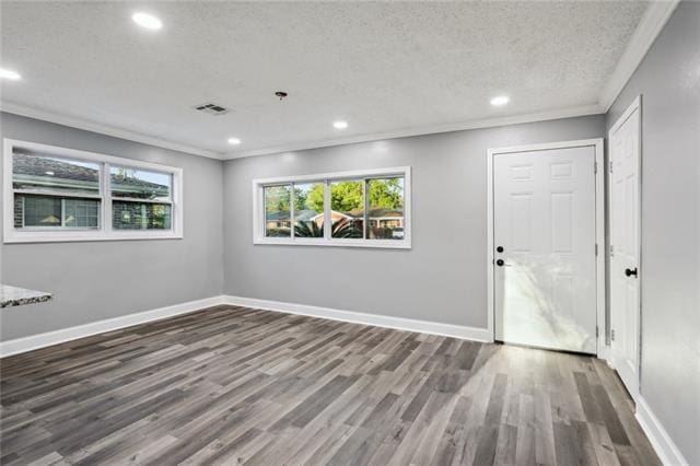 empty room with a textured ceiling, dark hardwood / wood-style floors, plenty of natural light, and ornamental molding