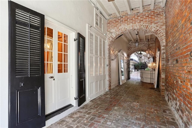 hallway featuring beamed ceiling and brick wall