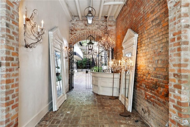 hallway featuring a towering ceiling, wood ceiling, brick wall, an inviting chandelier, and beamed ceiling