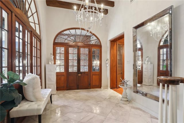 foyer with beamed ceiling, a notable chandelier, a towering ceiling, and french doors