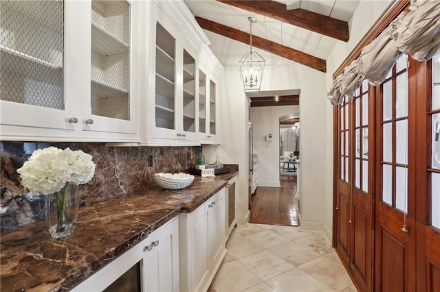 bar featuring decorative backsplash, dark stone countertops, white cabinetry, and hanging light fixtures